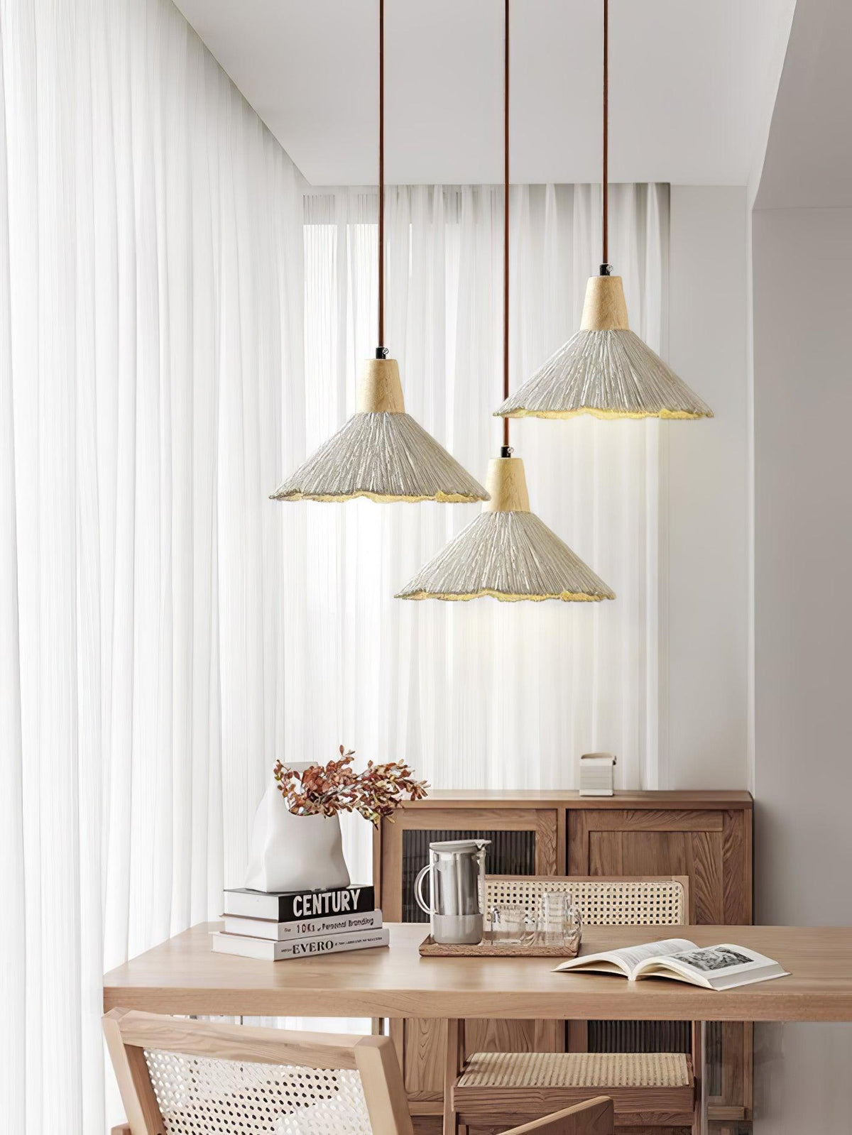 Three Clérachic pendants hang at different heights in front of sheer curtains, over a wooden sideboard and desk.