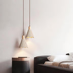 Two bell-shaped Clérachic pendants hang at different heights beside a dark bed and a copper-topped side table.