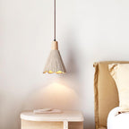 A Clérachic pendant with a bell shade hangs over a round stone side table, a golden bedhead behind it.