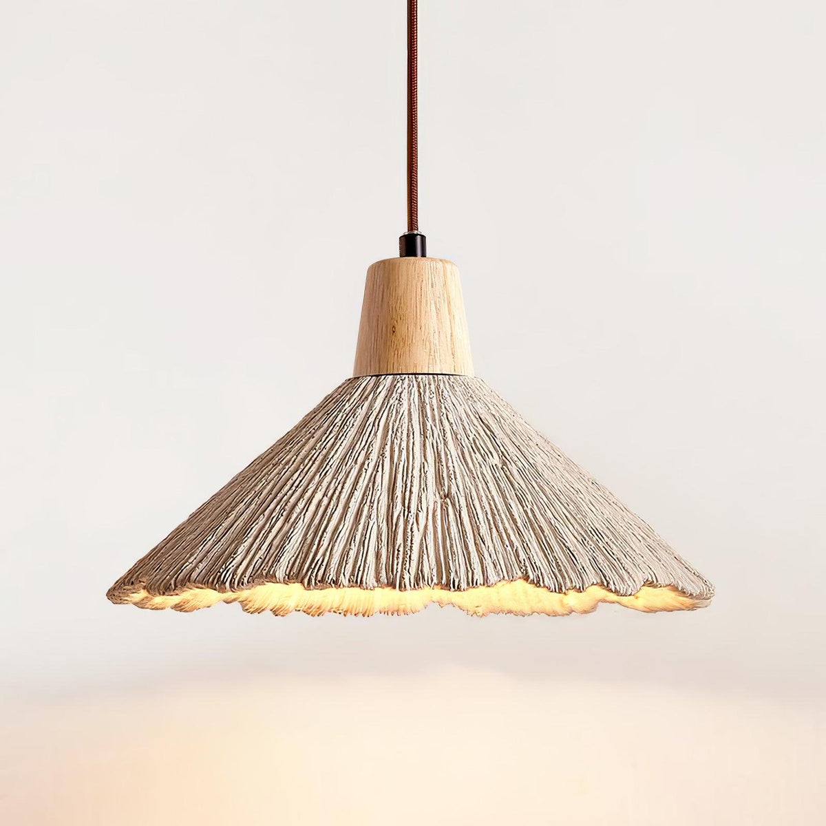 Close view of a wide-shade Clérachic pendant lit from within, its grey ridged surface and wood cap on a pale backdrop.