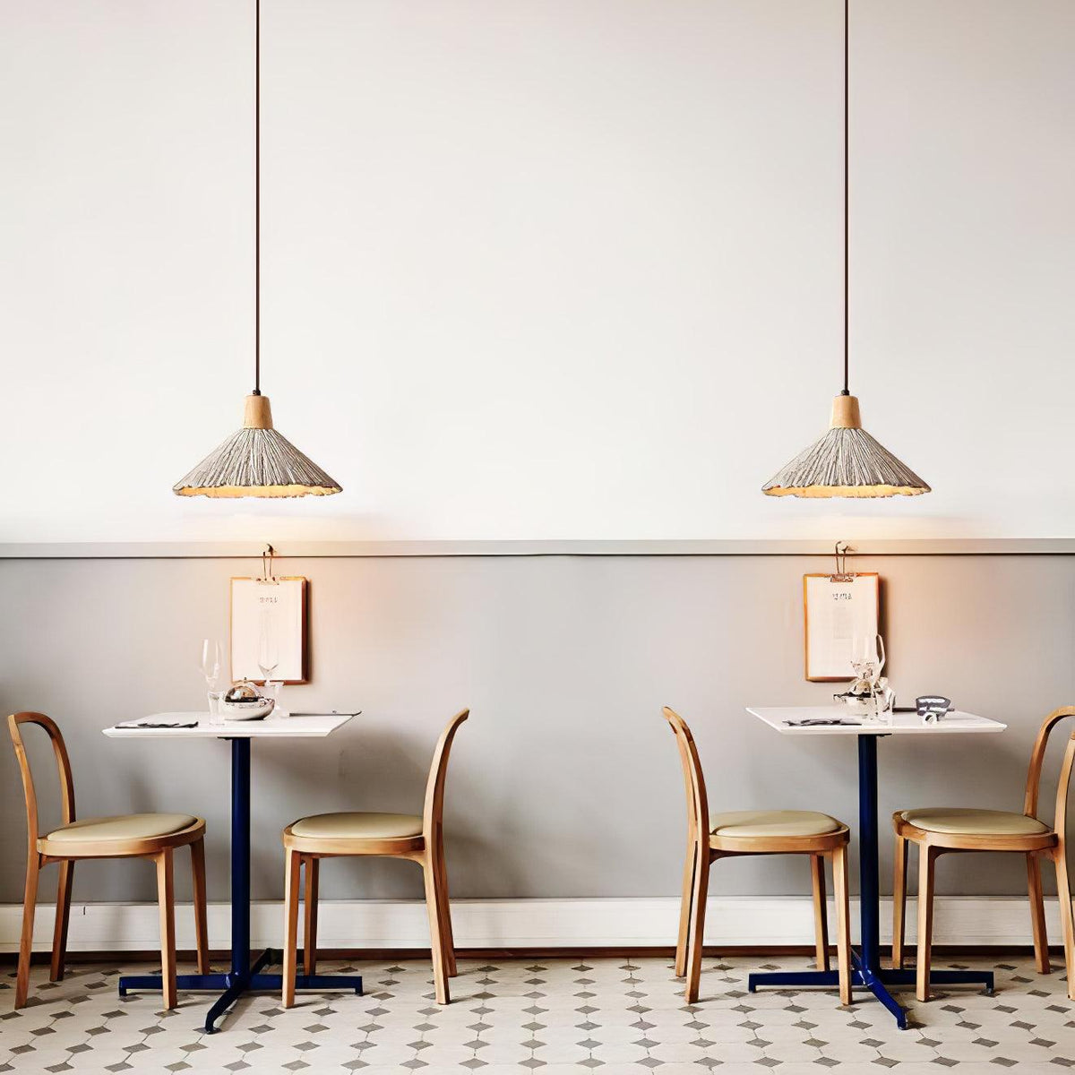 Two wide-shade Clérachic pendants hang over small café tables with wooden chairs and a tiled floor.