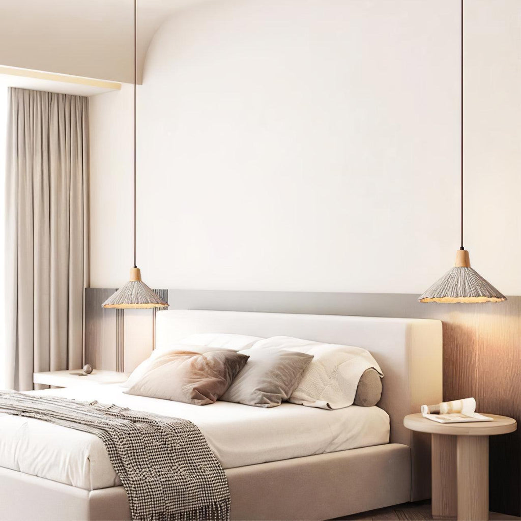 A wide-shade Clérachic pendant hangs on each side of a bed with a cream headboard, grey curtains and a round bedside table.