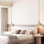 A wide-shade Clérachic pendant hangs on each side of a bed with a cream headboard, grey curtains and a round bedside table.