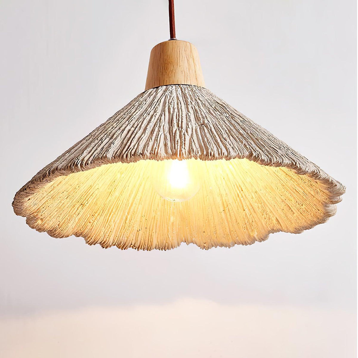 Seen from underneath, this Clérachic pendant's shade glows warm around a visible bulb, with a wooden cap and brown cord above.