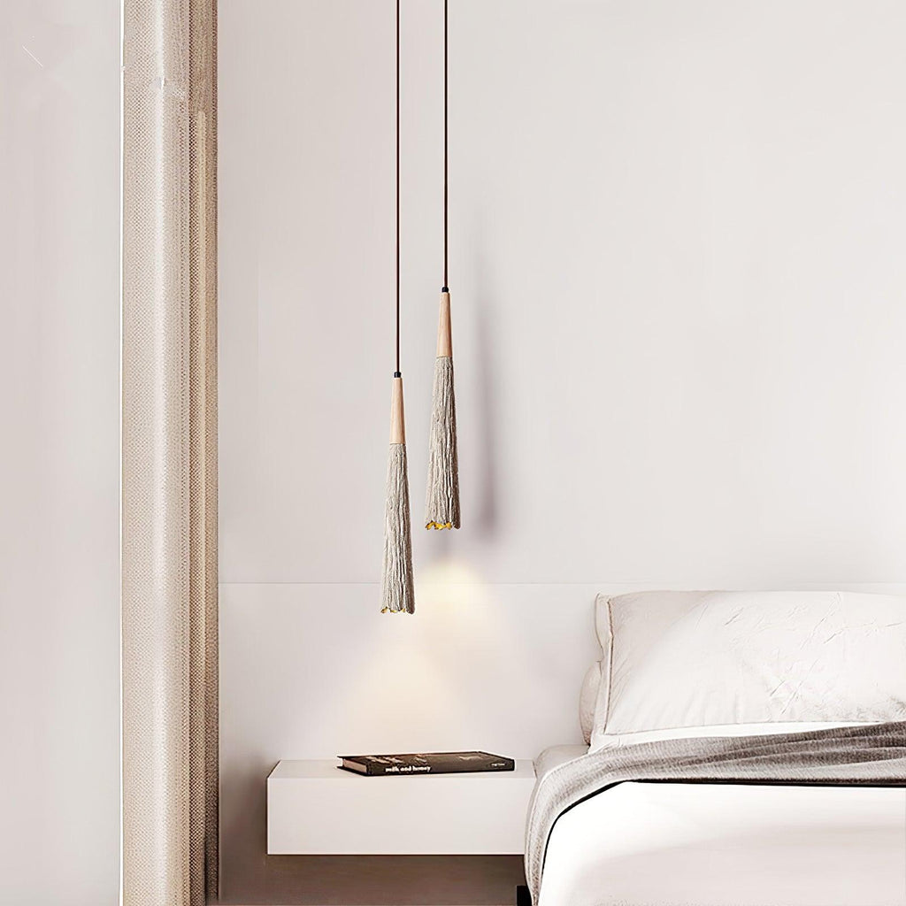 Two slim Clérachic pendants hang at different heights beside a floating shelf and a bed with grey bedding.