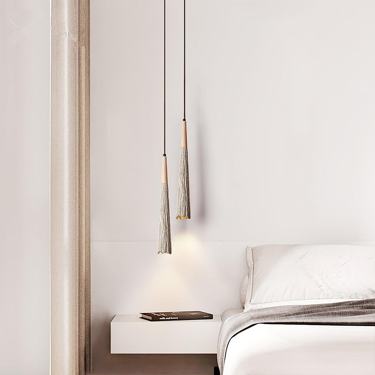 Two slim Clérachic pendants hang at different heights beside a floating shelf and a bed with grey bedding.