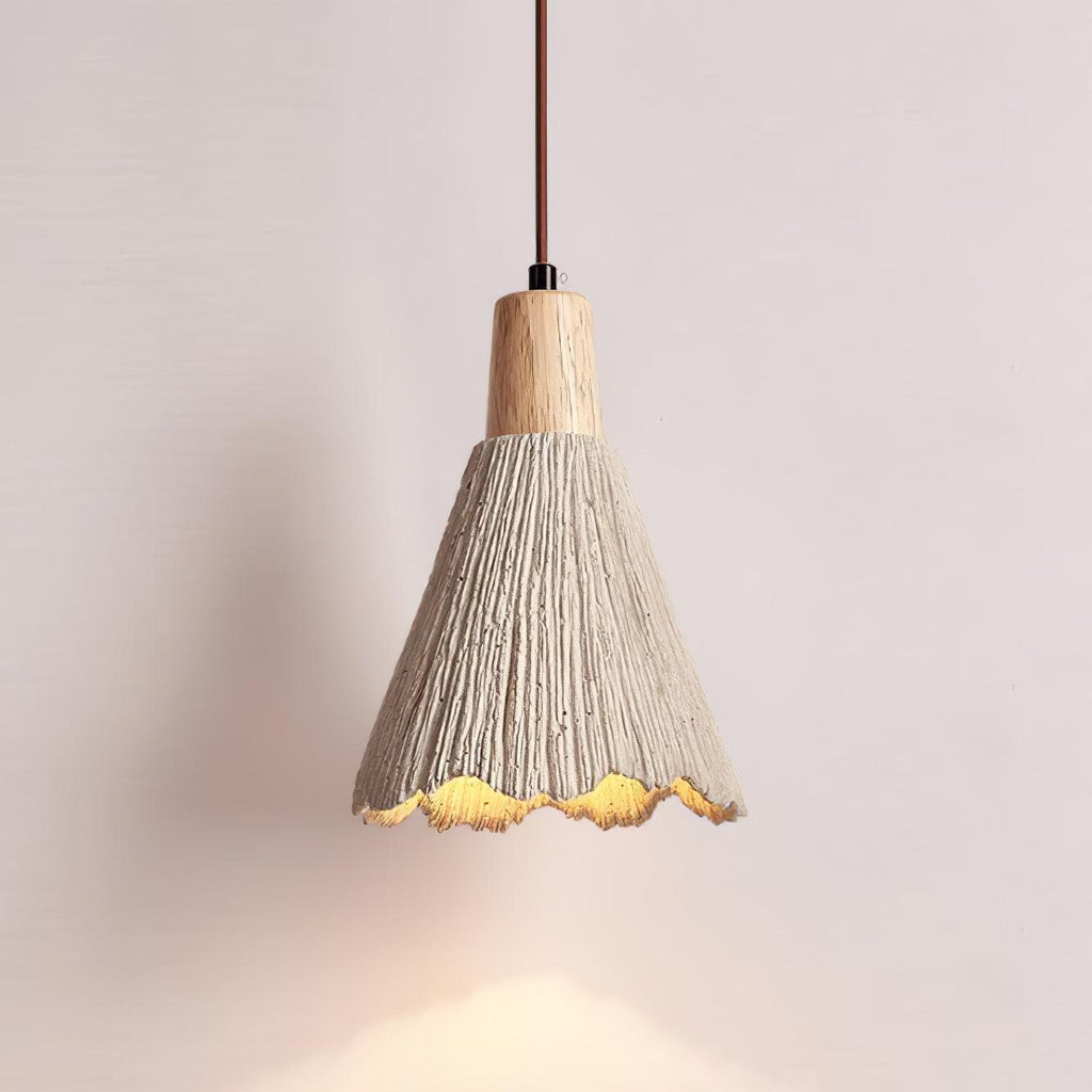 A bell-shaped Clérachic pendant glows against a pale pink wall, its scalloped rim lit warm below a wooden cap.