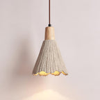 A bell-shaped Clérachic pendant glows against a pale pink wall, its scalloped rim lit warm below a wooden cap.