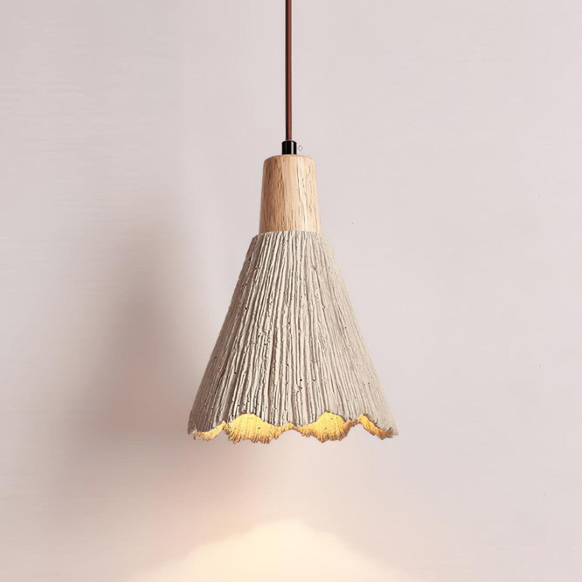 A bell-shaped Clérachic pendant glows against a pale pink wall, its scalloped rim lit warm below a wooden cap.