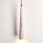 Close view of a long, narrow Clérachic pendant with a wooden top and a ridged grey tapered shade, lit at the tip.