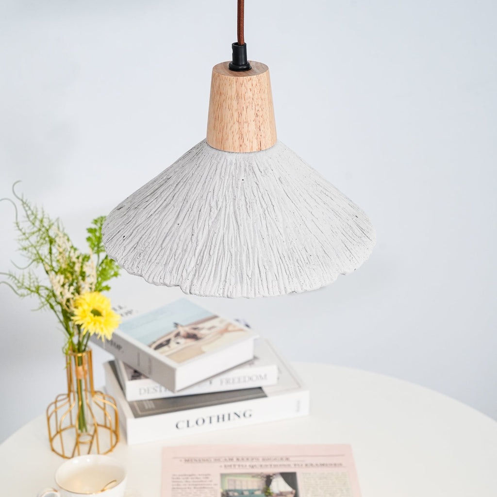 Only the underside of this Clérachic pendant shows over a white table with stacked books and a vase of yellow flowers.