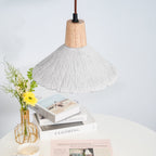 Only the underside of this Clérachic pendant shows over a white table with stacked books and a vase of yellow flowers.