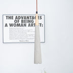 A slim Clérachic pendant hangs close to the camera in front of a large framed poster, with a flower vase below.