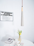A narrow Clérachic pendant hangs beside a framed print, over a white table with books, a teacup and a gold vase of flowers.
