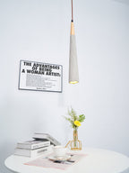 A slim Clérachic pendant glows at the tip, with a framed print behind it and books, a cup and flowers on a table below.