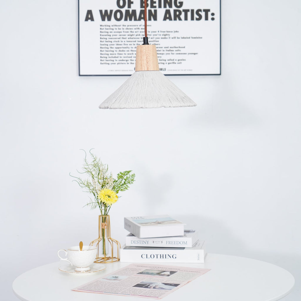 Part of a wide-shade Clérachic pendant at the top of the frame, with a framed print behind and a table of books and flowers below.