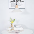 Part of a wide-shade Clérachic pendant at the top of the frame, with a framed print behind and a table of books and flowers below.
