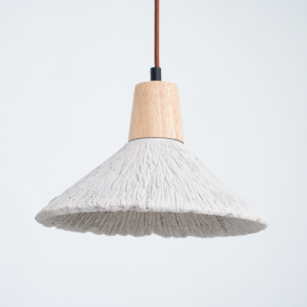 Close view of a wide grey Clérachic pendant with a wooden cap and a ridged shade, against a pale blue-grey background.