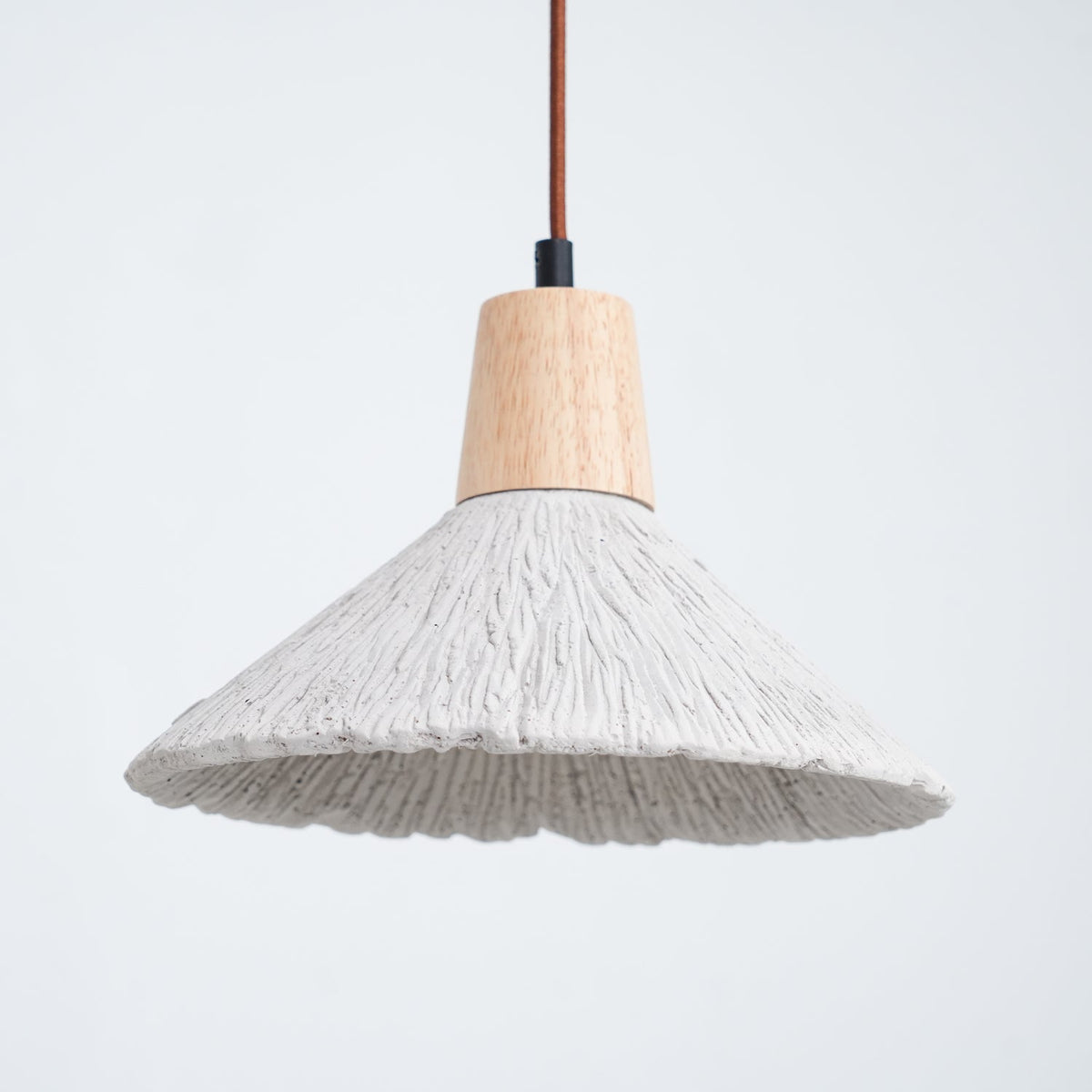 Close view of a wide grey Clérachic pendant with a wooden cap and a ridged shade, against a pale blue-grey background.