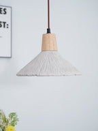 A smaller wide-shade Clérachic pendant hangs against a pale wall, with a corner of a framed print and flowers at the edge.