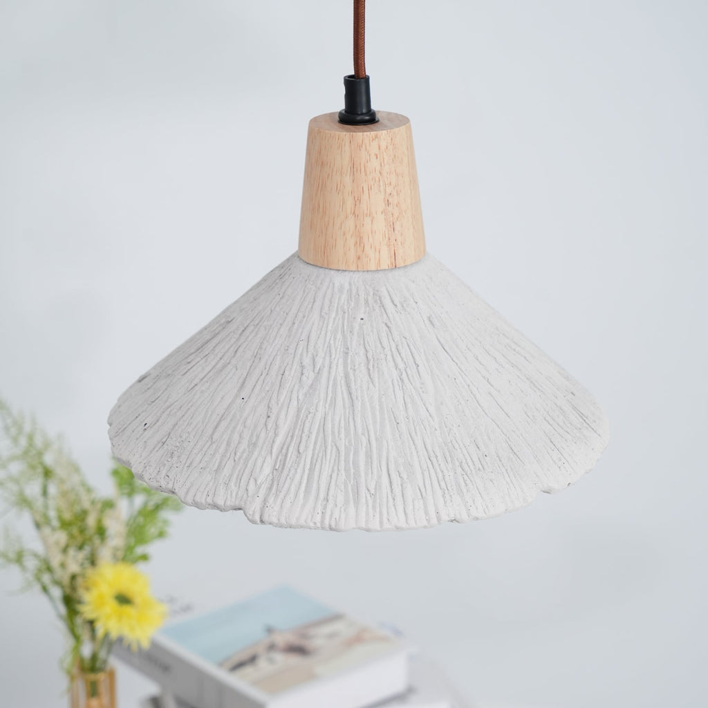 A wide-shade Clérachic pendant hangs over a table with books and yellow flowers, in soft daylight.