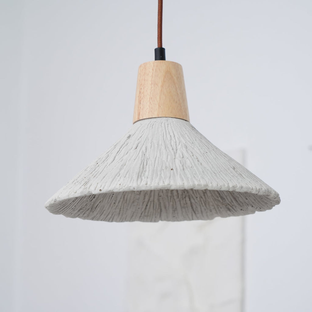 Close, slightly raised view of a wide grey Clérachic pendant with a wooden cap and a rough, ridged concrete-effect surface.
