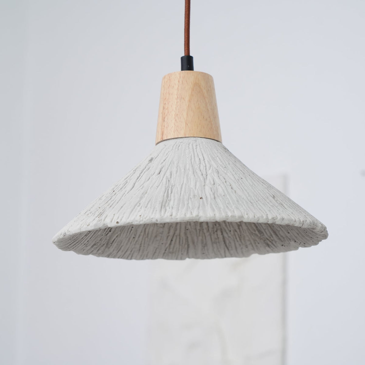 Close, slightly raised view of a wide grey Clérachic pendant with a wooden cap and a rough, ridged concrete-effect surface.