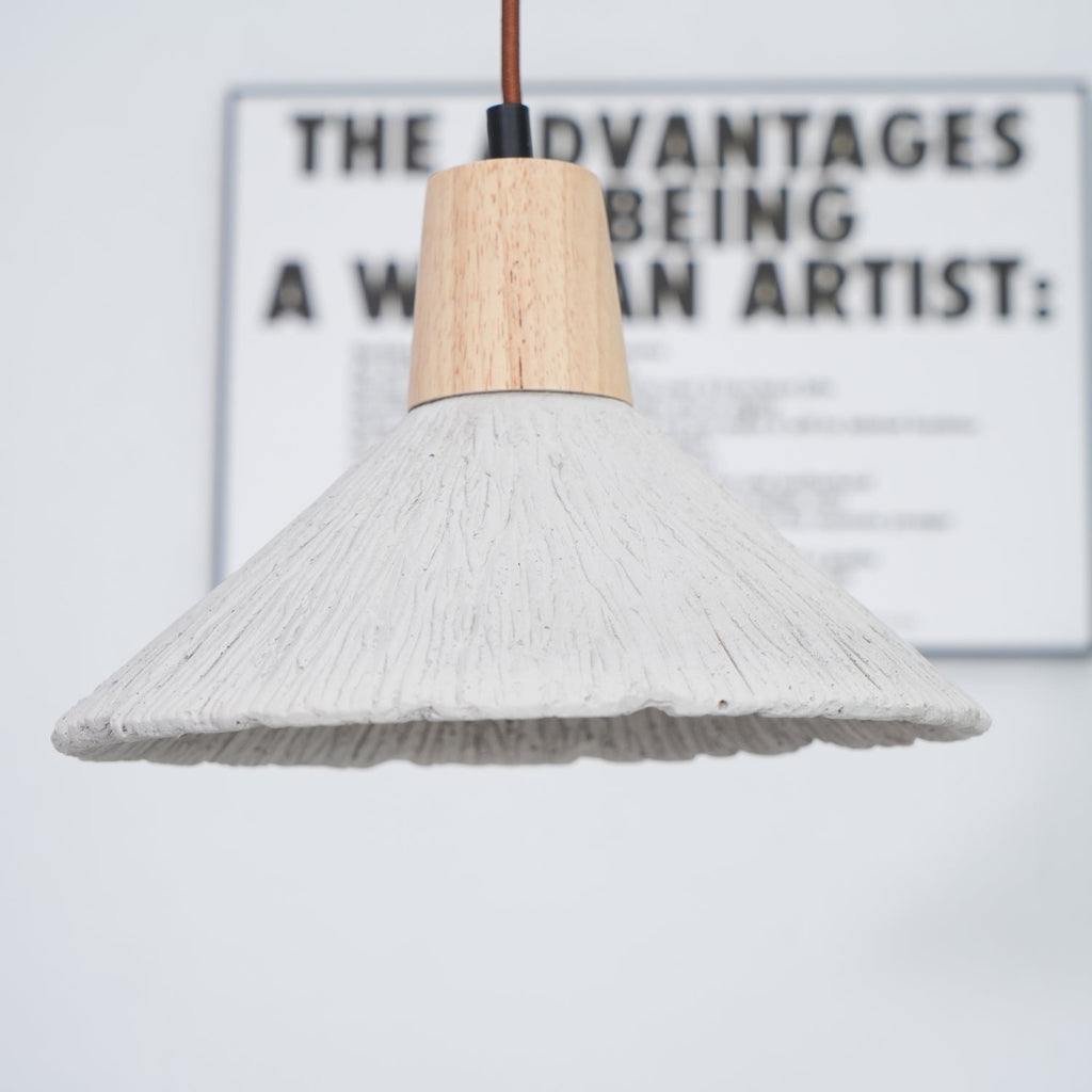 Wide grey Clérachic pendant in front of a blurred framed print, its wooden cap and ridged shade in sharp focus.