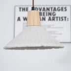 Wide grey Clérachic pendant in front of a blurred framed print, its wooden cap and ridged shade in sharp focus.