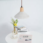 A wide-shade Clérachic pendant seen at a distance, hanging over a round table with a teacup, books and flowers.