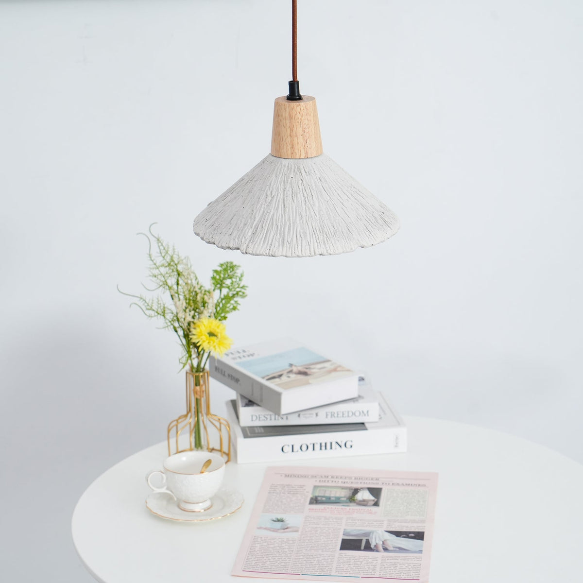 A wide-shade Clérachic pendant seen at a distance, hanging over a round table with a teacup, books and flowers.