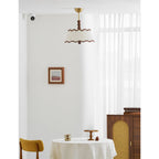 A Clérachic pleated ceiling light seen from a distance in a white room, with sheer curtains, a cane-fronted cabinet and a small round table.