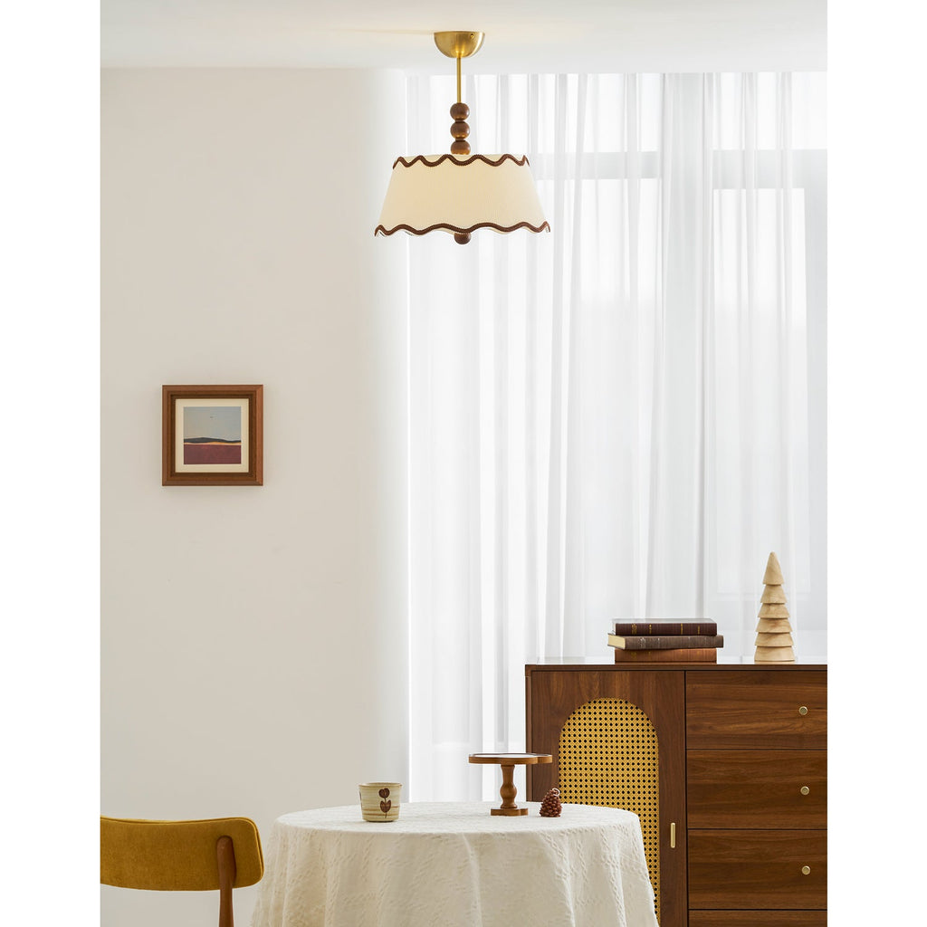 Clérachic pleated fabric ceiling light with wood beads in a bright room, with a framed print, a walnut cabinet and a table with a white cloth.
