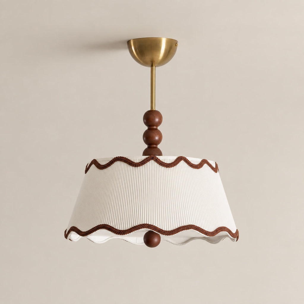 Close view of the wavy brown trim, pleated white shade, wood beads and brass canopy of this Clérachic ceiling light against a beige wall.