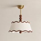 Close view of the wavy brown trim, pleated white shade, wood beads and brass canopy of this Clérachic ceiling light against a beige wall.