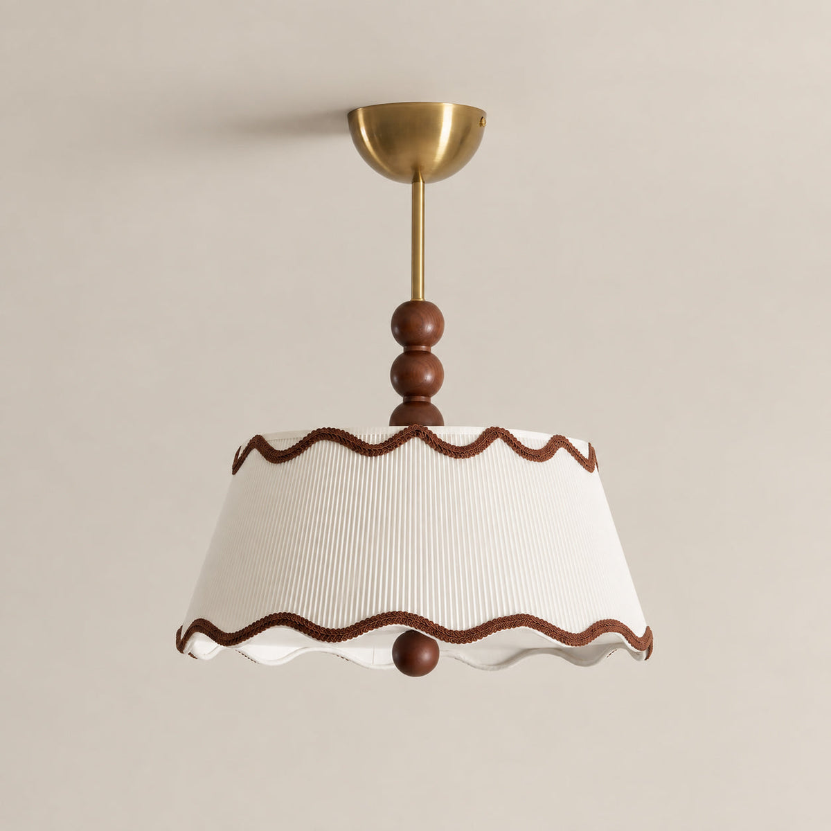 Close view of the wavy brown trim, pleated white shade, wood beads and brass canopy of this Clérachic ceiling light against a beige wall.