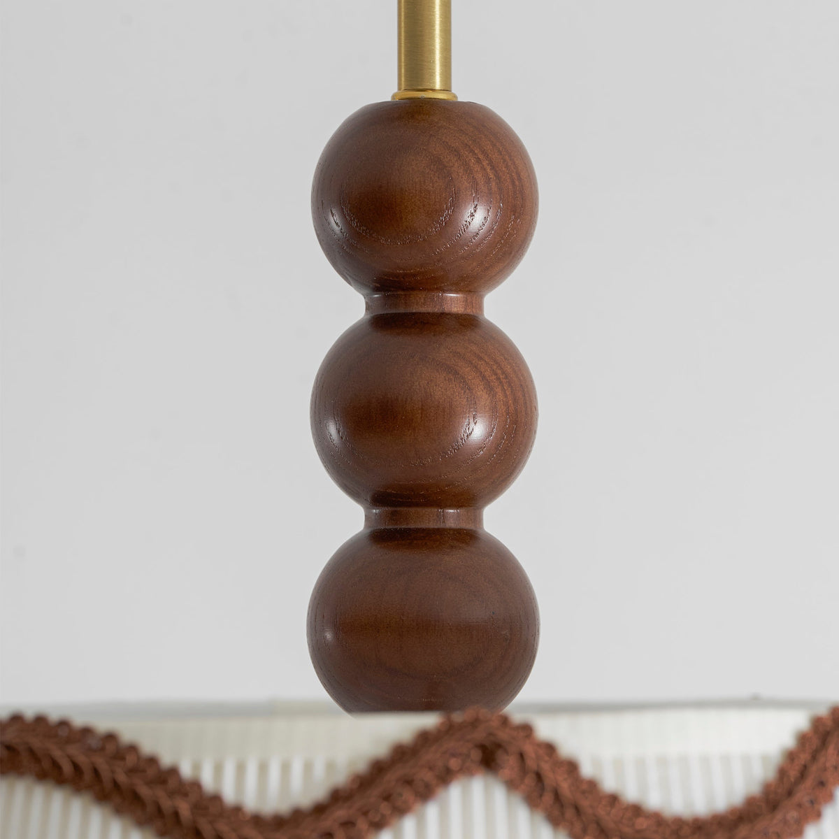 Close view of three stacked walnut beads on the stem of this Clérachic ceiling light, with the pleated shade edge below.