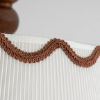 Close view of the wavy brown braid trim on the pleated white shade of this Clérachic ceiling light.