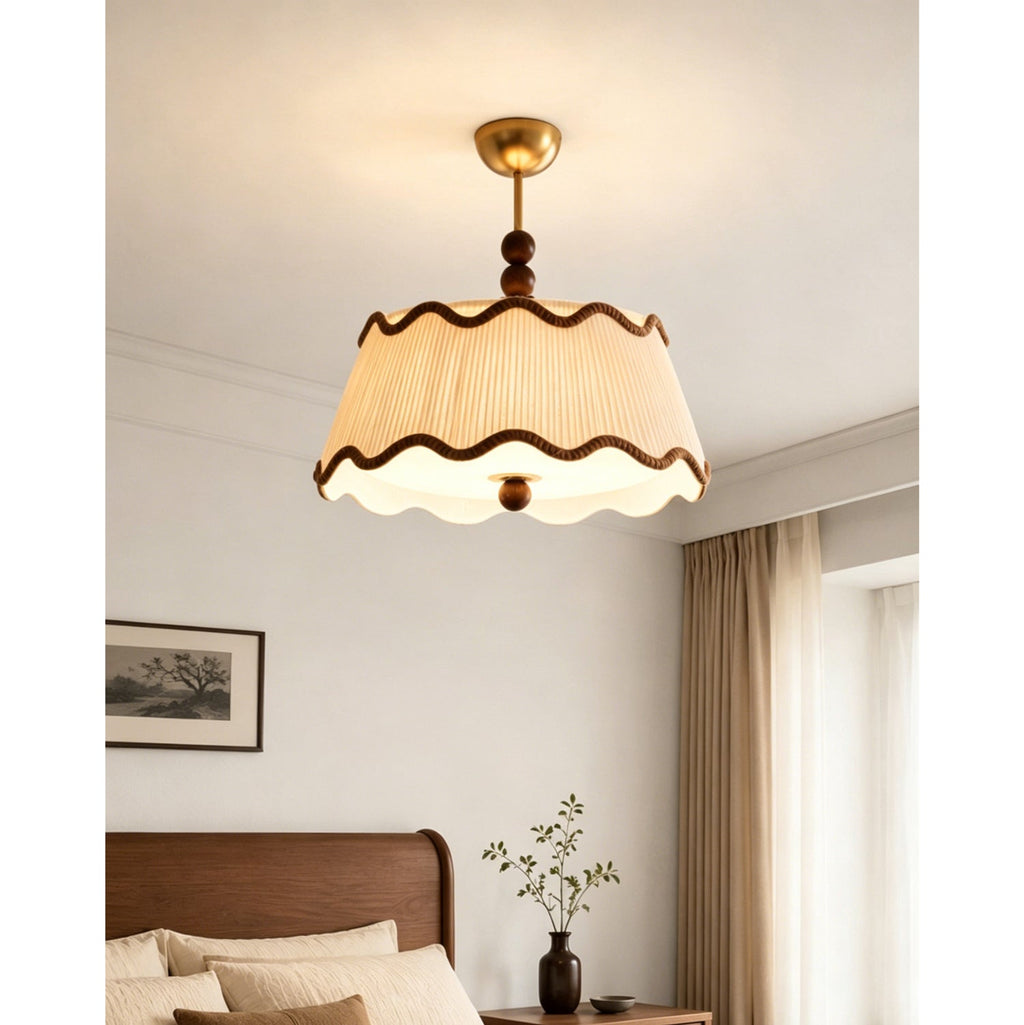 Clérachic ceiling light with a lit pleated shade above a bedside table with a dark vase, in a bedroom with long curtains.