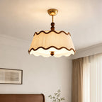 Clérachic pleated ceiling light lit from below, with the scalloped diffuser visible and a framed print and curtains behind.