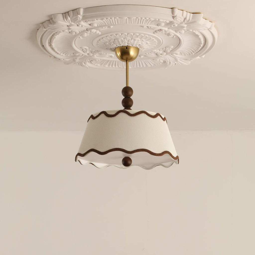 Unlit Clérachic pleated ceiling light hanging from a brass canopy beneath an ornate white plaster ceiling rose.
