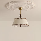 Unlit Clérachic pleated ceiling light hanging from a brass canopy beneath an ornate white plaster ceiling rose.