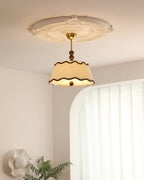 Lit Clérachic ceiling light under a plaster rose, with an arched white wall, sheer curtains and a green fern in the corner.