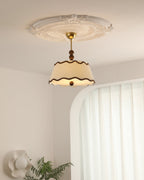 Clérachic pleated ceiling light seen from a distance below a plaster ceiling rose, in a room with an arched alcove and a fern.