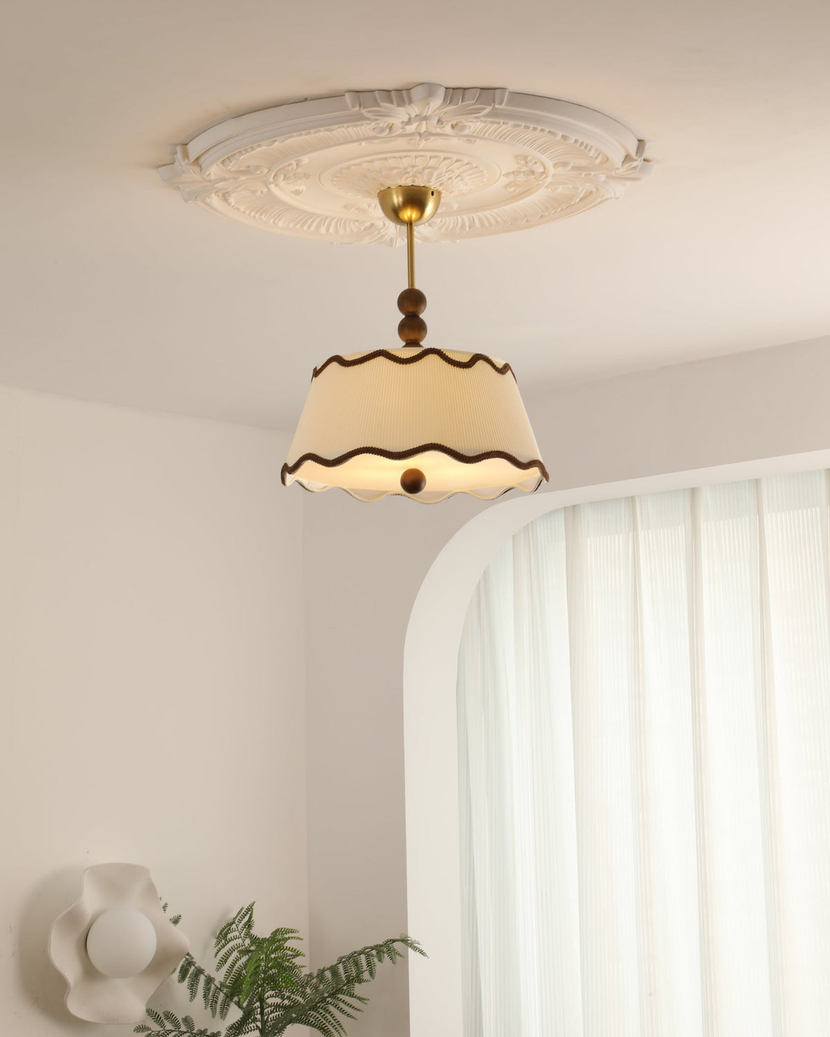Clérachic pleated ceiling light seen from a distance below a plaster ceiling rose, in a room with an arched alcove and a fern.