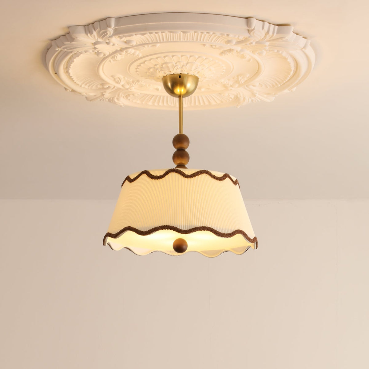 Close, lit view of a Clérachic pleated ceiling light with brass canopy beneath a large plaster ceiling rose.
