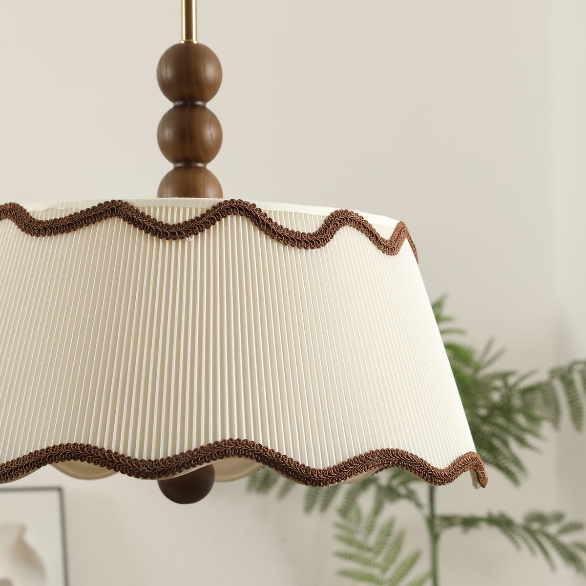 Close view of the pleated shade, its wavy brown trim and the walnut beads above it on this Clérachic ceiling light, with a fern behind.