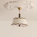 Unlit white Clérachic ceiling light with wavy brown trim beneath a carved plaster ceiling rose, from a low angle.