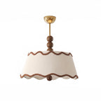 Front view of the white pleated Clérachic ceiling light with a scalloped hem and a wood bead below, on a white backdrop.