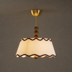 Lit Clérachic pleated ceiling light with brown trim and a brass canopy, glowing warm against a dark taupe wall.